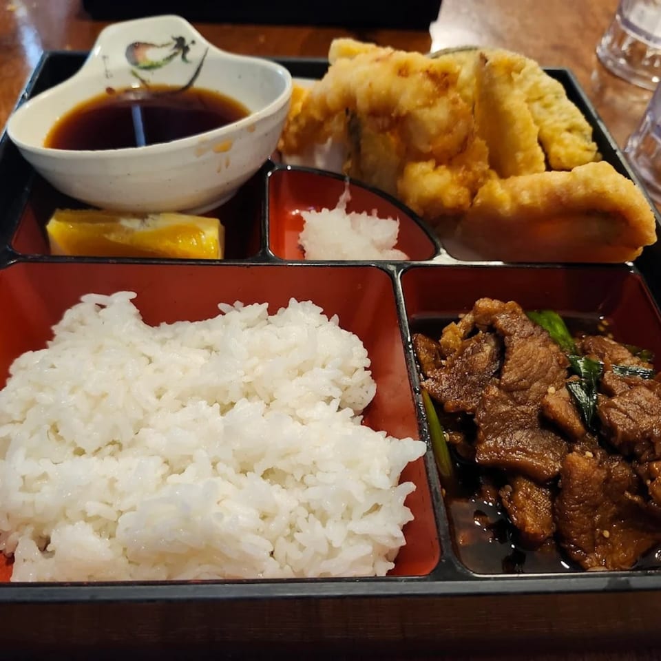 A Japanese bento box with tempura, beef, white rice, and dipping sauce.
