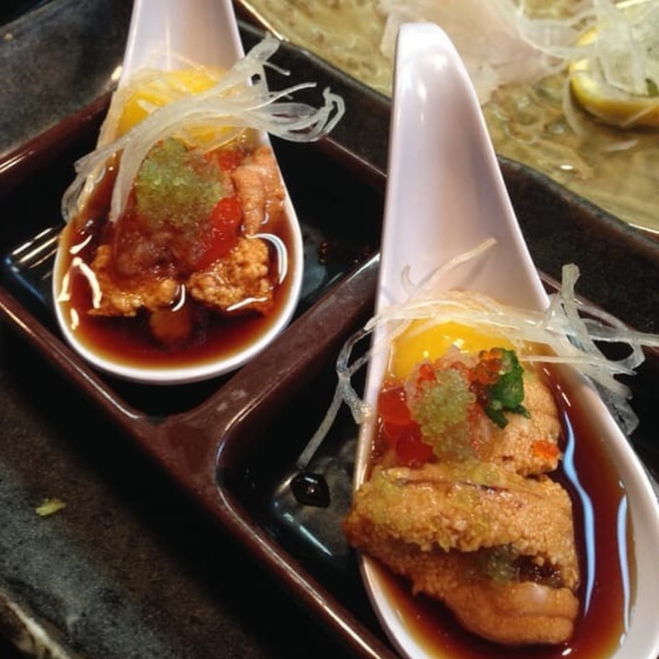 Two spoons of Japanese uni, salmon roe, and quail egg in a dark sauce.