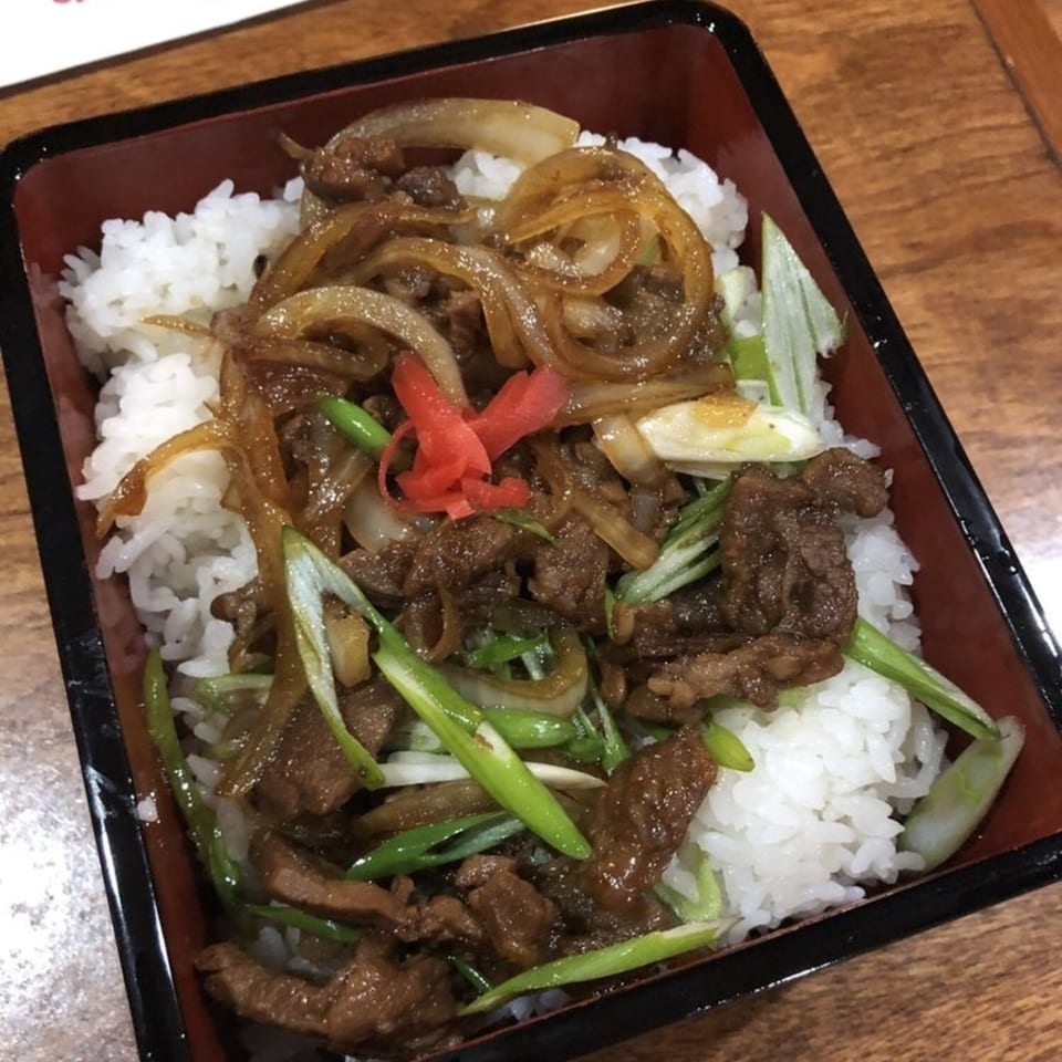 Japanese beef and onion donburi with white rice, green onions, and red ginger in a black bowl.