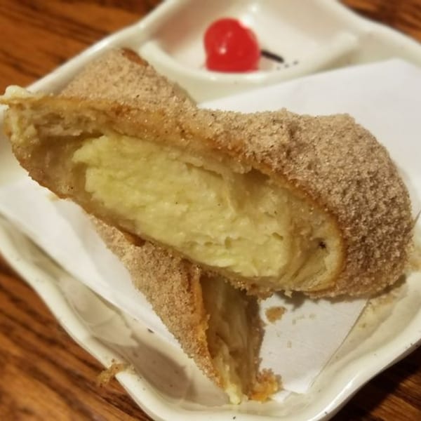 A golden-brown dessert, cut in half, revealing a creamy yellow filling, dusted with cinnamon sugar.