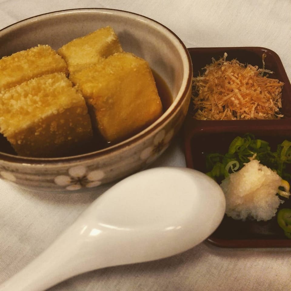 A bowl of agedashi tofu with broth, a side of bonito flakes, and grated daikon with scallions.