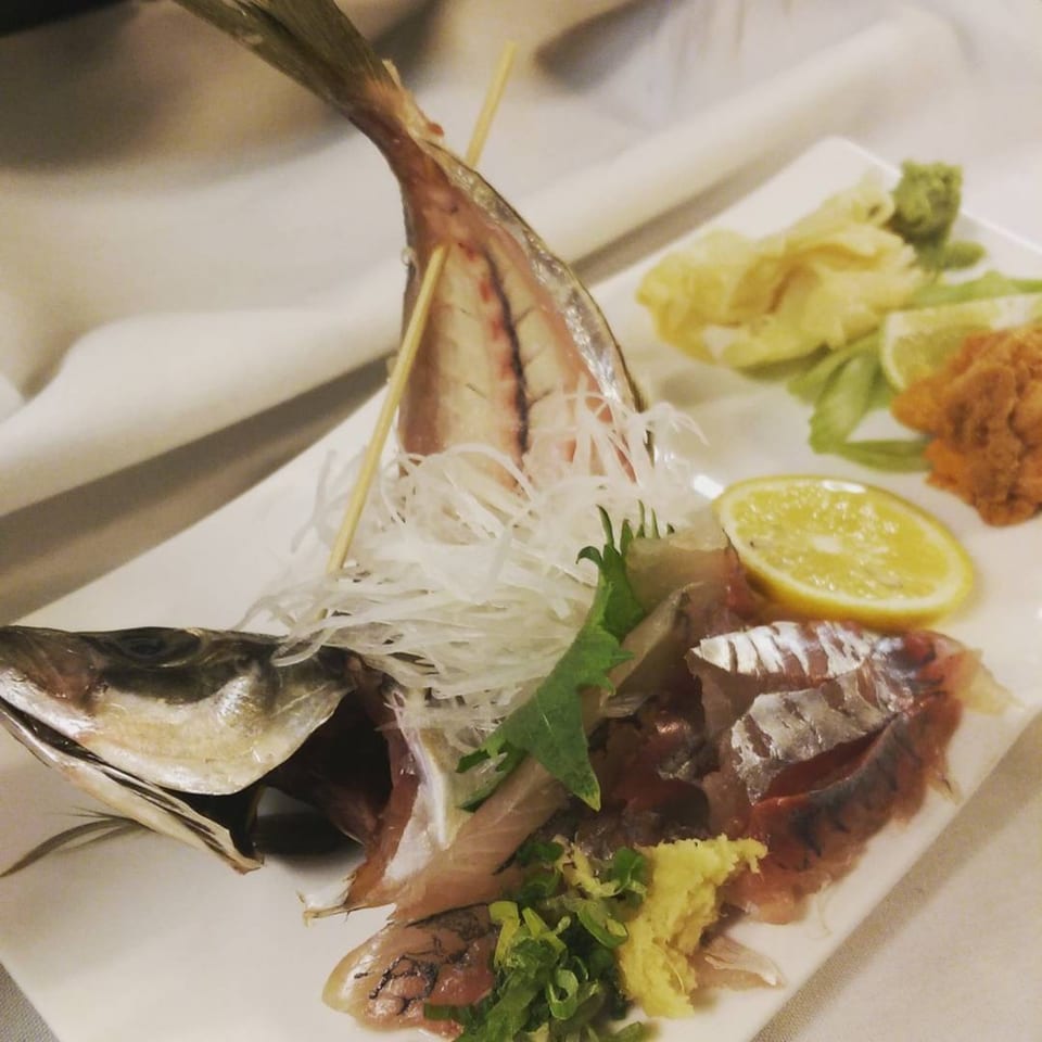 Whole fish sashimi with shredded daikon, lemon, and ginger on a white plate.